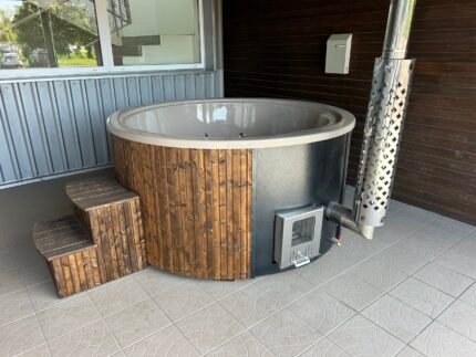 Brit Hot Tubs - Immerse Yourself in Luxury with the HARMONIA Deluxe Acrylic Hot Tub Escape the stresses of everyday life and indulge in the lap of luxury with the HARMONIA Deluxe Acrylic Hot Tub. Priced at £4,700 this exquisite 4-6 seater hot tub is designed to bring the ultimate spa experience right to your backyard, elevating your relaxation to new heights. Step into a world of sophisticated comfort and advanced features that will leave you feeling rejuvenated, both physically and mentally. Whether you're seeking a tranquil sanctuary for personal rejuvenation or a gathering place to create cherished moments with loved ones, the HARMONIA is the perfect addition to your outdoor living space. HARMONIA Deluxe Acrylic Hot Tub Compact Yet Spacious Design Boasting an internal diameter of 180 cm and an external diameter of 201 cm, the HARMONIA hot tub comfortably accommodates up to 6 people. The ergonomic bench seating, featuring a height of 27 cm and width of 36 cm, ensures maximum comfort and support for all users, allowing you to sink into a state of pure bliss. Premium Acrylic Construction Crafted from high-quality acrylic, the HARMONIA hot tub exudes a sleek, modern aesthetic that complements any outdoor setting. Choose from a variety of insert colors, including Grey, Blue, White, or Gold, to seamlessly blend with your personal style. The durable acrylic construction not only enhances the overall look but also makes maintenance a breeze. Efficient and Eco-Friendly Heating At the heart of the HARMONIA lies an external integrated wood-burning oven, crafted from premium AISI 316 stainless steel with a powerful 30kW output. This impressive heating system warms the water in just 1.5 to 2 hours, ensuring you can start your relaxation journey without delay. The glass heater door allows for easy monitoring, while the Stainless Steel, Grey, or Black finish options let you personalize the oven to your taste. Therapeutic Hydrotherapy Indulge in the HARMONIA's advanced hydrotherapy features, designed to soothe and rejuvenate. Experience the targeted massage of 10 powerful hydro jets and the gentle, effervescent caress of 12 air bubble jets. Set the perfect mood with the 4 main LED lights and mini LED lights inside and outside the tub, creating a spa-like ambiance. Comfort and Convenience Your comfort is our priority. The HARMONIA comes equipped with 6 headrests to provide additional support, allowing you to fully unwind and immerse yourself in the therapeutic benefits of the hot tub. Thoughtful features like the stainless steel chimney, high-flow drain tap, thermo cover, and sand filter system ensure easy maintenance and year-round enjoyment. Create Your Personal Oasis Elevate your outdoor living experience and transform your backyard into a haven of luxury and relaxation. The HARMONIA Deluxe Acrylic Hot Tub is more than just a purchase; it's an investment in your well-being and the creation of cherished memories with family and friends. Don't settle for anything less than the ultimate in comfort and style. Order the HARMONIA Deluxe Acrylic Hot Tub today and unlock a world of unparalleled relaxation right in the comfort of your own home. HARMONIA HOT TUB SPECIFICATIONS High-quality acrylic insert Wood cladding walls Integrated wood-fired heater  Internal width 165 cm  External width 200 cm  Capacity: 4-6 person Inside height 88 cm; External height 105 cm Water capacity: 1200-1300 L Empty weight 180kg 1.5h – 2h heating time Insert insulated with polyurethane foam Glass heater door Stainless steel chimney 2m with a cap Chimney heat guard Hydro massage and air bubble system with 8 jets Air bubble system with 12 jets Underwater MINI LED lights Exterior LED light stripe Insulated Thermo lid  2 drink holders - stainless steel Box stair Stainless steel drain valve 40mm Sand filter 24 months warranty Colour of ergonomic acrylic insert available: Grey, Beige, White Stainless steel wood burning oven ( AISI 304) 30 kW or (AISI 316) 30 kW Oven front colour: Stainless steel – GREY, or Stainless steel - BLACK Wall cladding: Pine Wood - thickness 20 mm, Thermo Wood - thickness 20 mm, UPVC - thickness 18mm, Cedar Wood - thickness 18 mm Wood cladding stain colours: Transparent Grey, Transparent Brown, Teak, and Black Insulated Thermo lid colours: grey or brown Do you have more QUESTIONS about Harmonia DELUXE acrylic hot tub? Contact our sales team now! Here you can find alternative hot tubs.